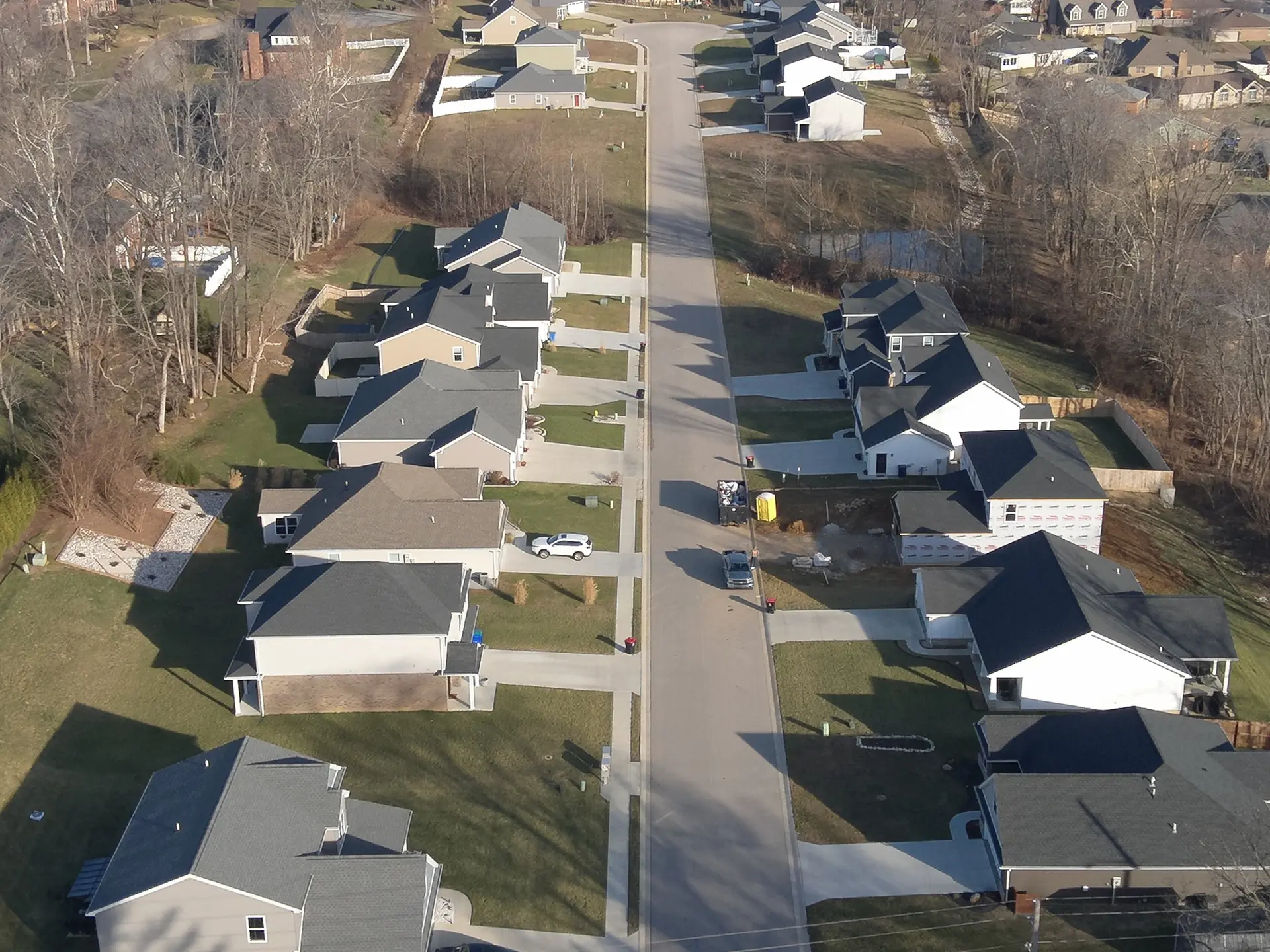 Aerial view of a street of new single-family homes with gray roofs on tree-lined lots, one home still under construction, in a Reinbrecht Homes neighborhood.